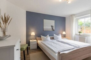 Een slaapkamer met een bed, nachtkastjes, een raam en een aan de muur hangend schilderij.