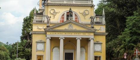 A yellow building with columns and statues, a sign reading 'Gloriosa Dicta Sunt De Te', and a parked car in front.