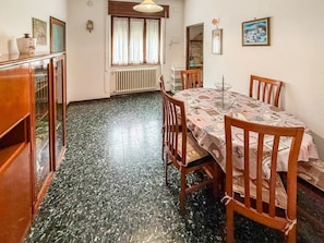 A dining area with a table set for four, wooden chairs, a radiator, and a window with curtains. - 5 Minutes from La Godorta (Gozzano)