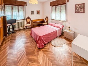 A bedroom with a herringbone floor, a bed with a red polka dot bedspread, a wooden desk with a computer, and a radiator. - 5 Minutes from La Godorta (Gozzano)