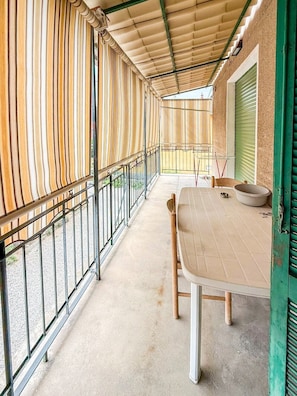 A covered outdoor seating area with a table and chairs, a metal railing, and a view of the street. - 5 Minutes from La Godorta (Gozzano)