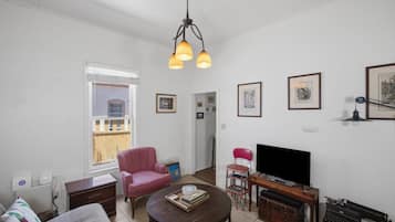 A living room with a sofa, a pink chair, a wooden coffee table, a TV, and a bookshelf.