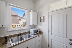 Una cocina con un lavamanos doble, un microondas y una ventana con vistas a una casa.