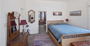 Un dormitorio con cama de madera, cómoda, espejo y puerta que da a un baño.