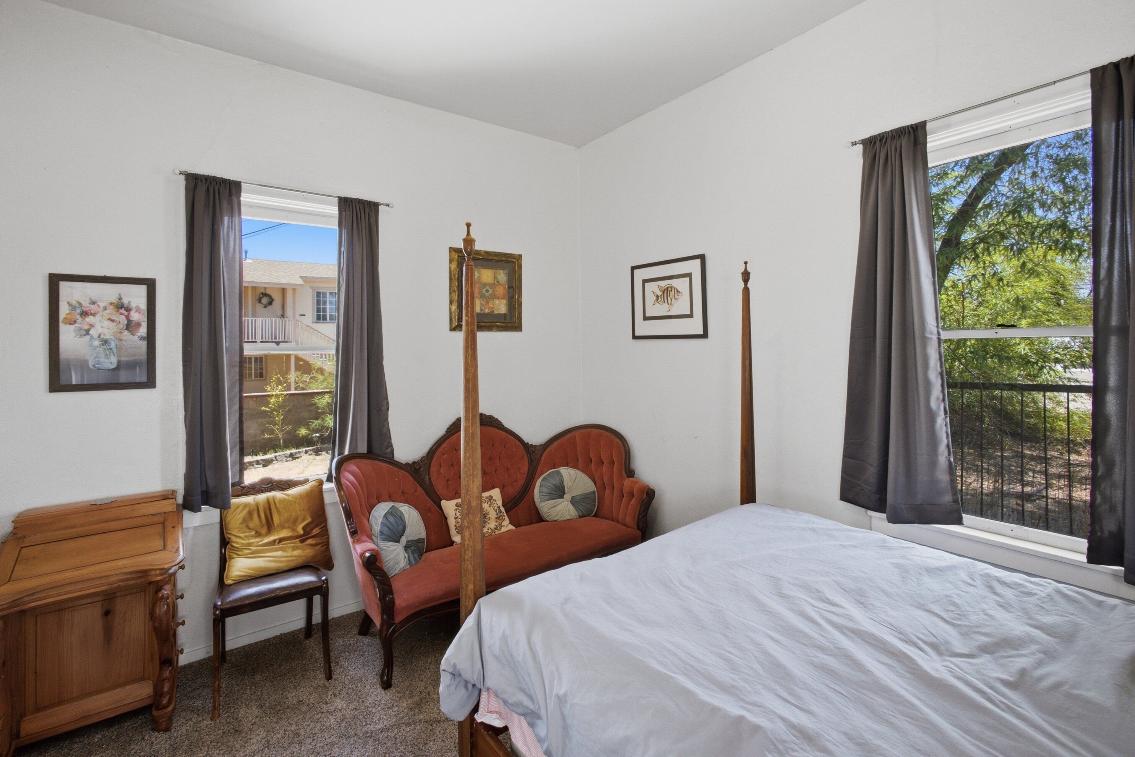 Une chambre à coucher avec un lit, une chaise, une table en bois et une fenêtre avec des rideaux.