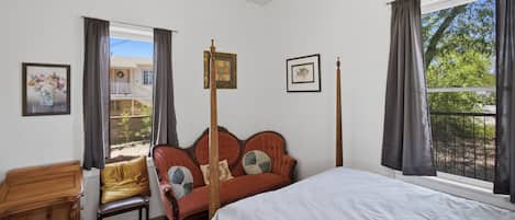 A bedroom with a bed, a chair, a wooden table, and a window with curtains.