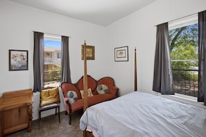Quarto com cama, cadeira, mesa de madeira e janela com cortinas.