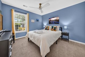 A bedroom with a bed, a nightstand, a desk, and a window with blinds. - 64a Ninth & Ivey Retreat 3 Bedroom Condo (Pawleys Island)