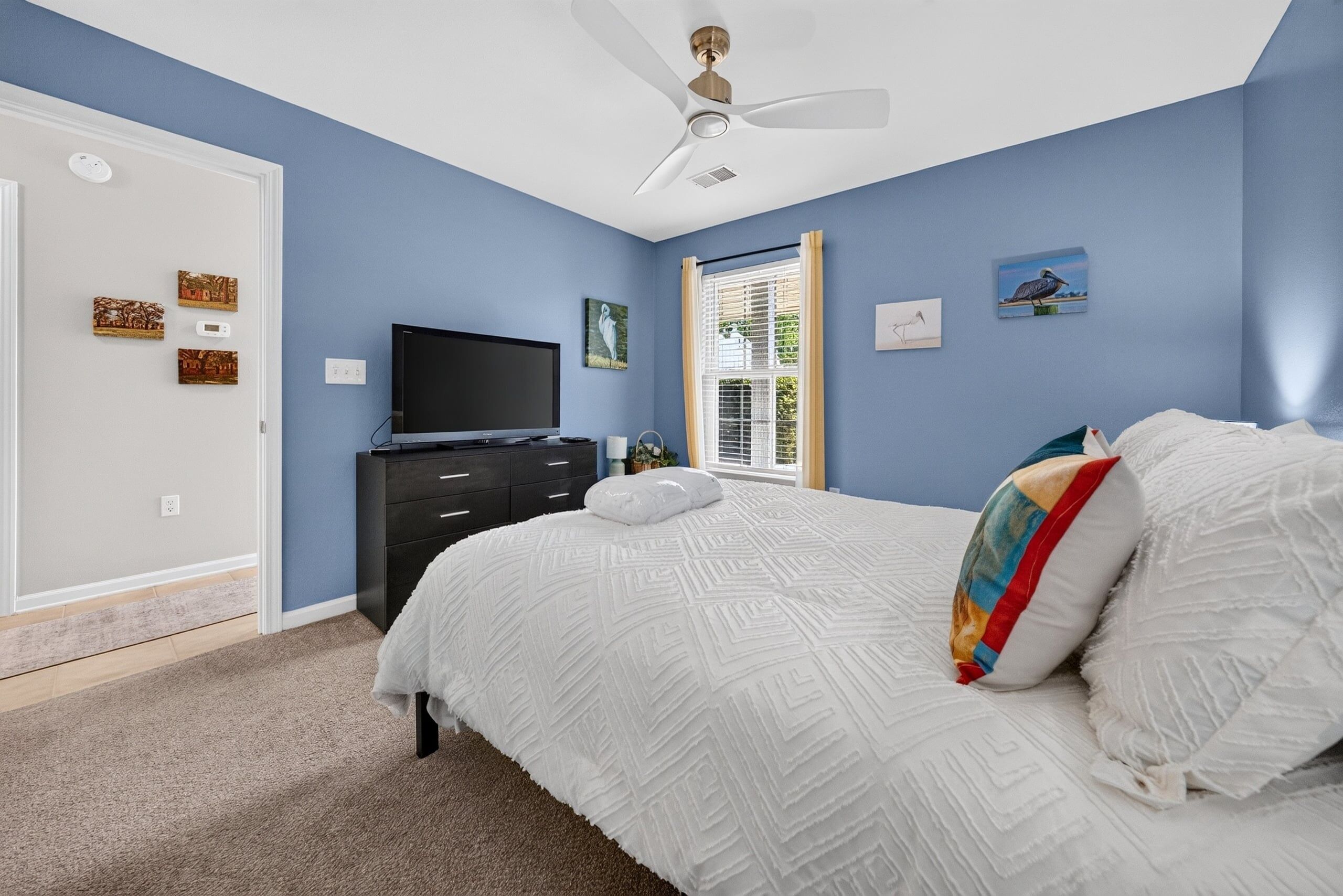 A bedroom with a bed, a television, a ceiling fan, and artwork on the walls.