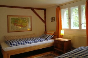 Ein Zimmer mit einem Bett, einem kleinen Tisch mit Lampe, einer Karte an der Wand und einem Fenster mit Vorhängen.