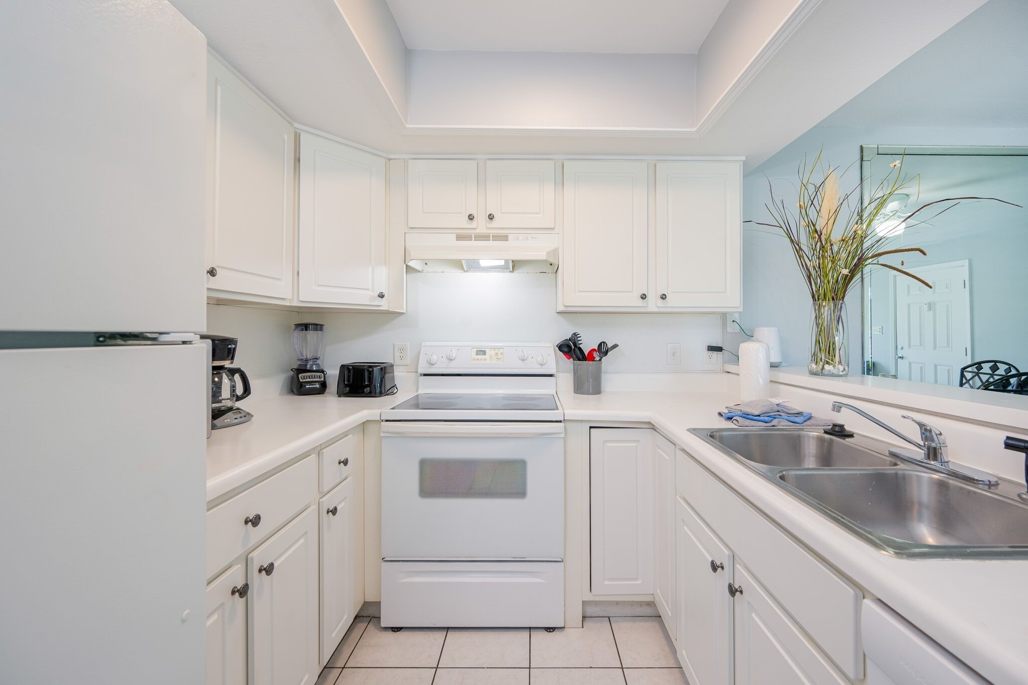 A modern kitchen with white cabinetry, a built-in oven, a coffee maker, and a sink.