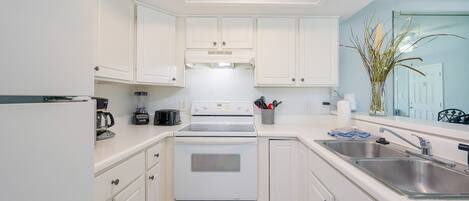A modern kitchen with white cabinetry, a built-in oven, a coffee maker, and a sink.