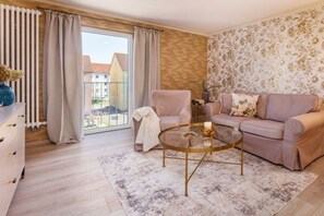 Ein Wohnzimmer mit einer Couch, einem Sessel, einem Glastisch und Blick durch ein großes Fenster.