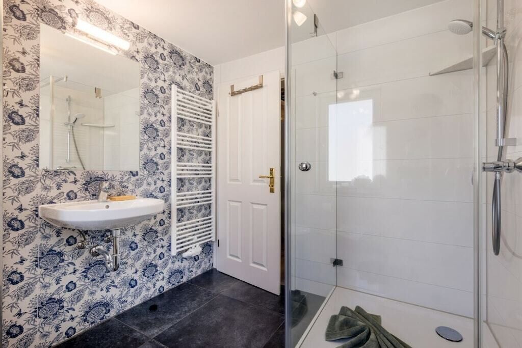Ein Badezimmer mit Duschkabine aus Glas, einem weißen Waschbecken und einer Wand mit Muster.