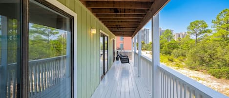 A covered wooden deck with a view of a beach and buildings in the distance.