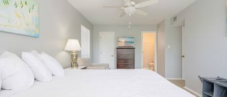 A bedroom with a large bed, a ceiling fan, a dresser, and a painting on the wall.