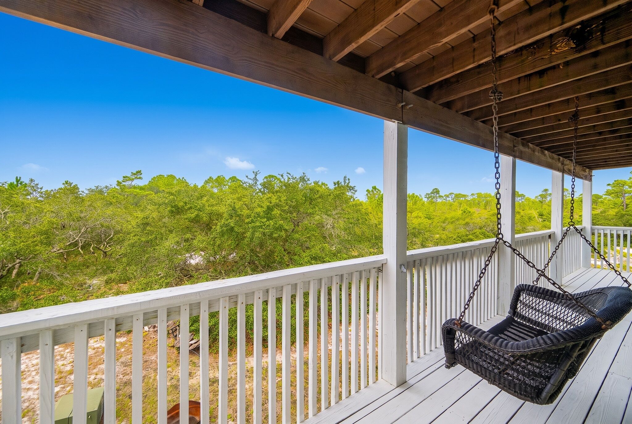 A wooden deck with white railings and a hanging chair.