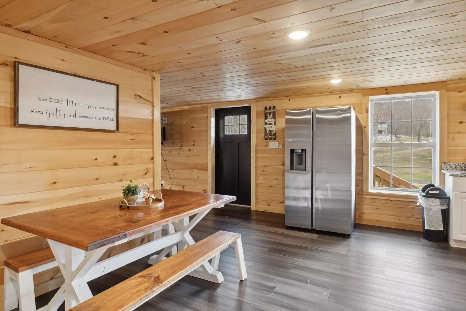 Interior de madera con una mesa y banco de madera, un refrigerador y una ventana con vistas.