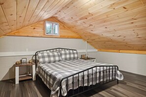 Een enkel bed met een geruit beddegoed in een kamer met houten balken en een klein raam.