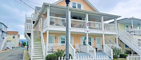 A multi-story building with a porch, a staircase, and a white picket fence.