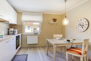 A kitchen with white cabinets, a dining table with a chair, a clock, and a hanging light fixture. - Miss Helma by the Sea, House Seagold (Saßnitz)