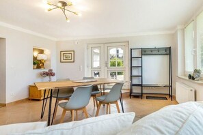 A modern room with a dining table, chairs, a bed, a wardrobe, and a window with blinds. - Holiday apartment in Binz with swimming pool (Binz)