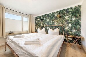 A bedroom with a bed, a nightstand, a window with curtains, and a wall with a nature-themed wallpaper. - Holiday apartment in Binz with swimming pool (Binz)