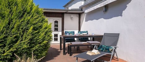 Une terrasse extérieure avec une table, des chaises et un fauteuil de relaxation.