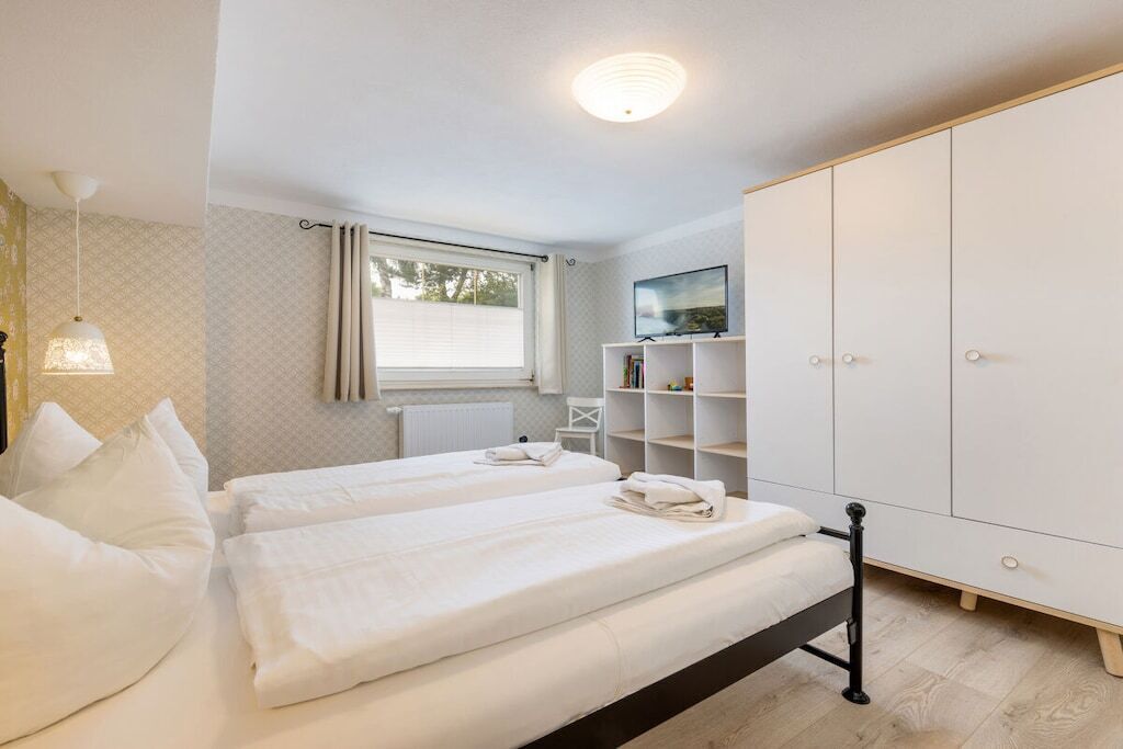 Une chambre avec deux lits, une armoire, un téléviseur et une fenêtre avec des rideaux.