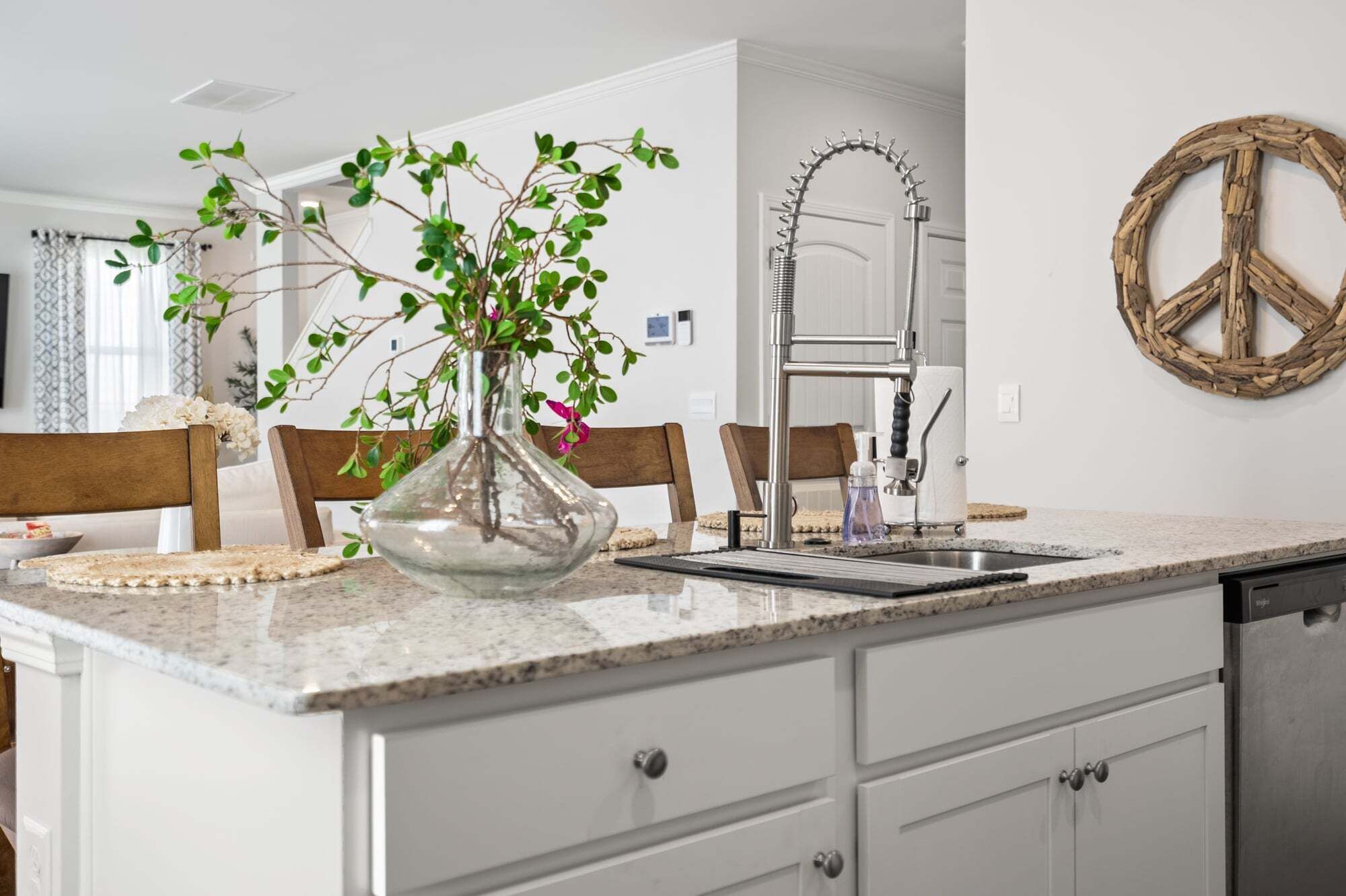 A kitchen with a granite countertop, white cabinetry, a stainless steel sink, and a vase with green plants.