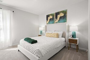 Een netjes ingerichte slaapkamer met een bed, twee nachtkastjes, een wandlamp en twee aan de muur bevestigde schilderijen.