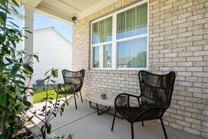 An outdoor patio with two black wicker chairs and a small round table, a brick wall, and a window with a green curtain. - Cozy 3BR Retreat Near Six Flags & Atlanta (Lithia Springs)