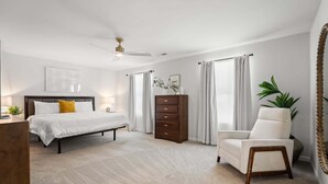 Ein Schlafzimmer mit einem Bett, einem Schminktisch, einem Sessel und einem Deckenventilator.