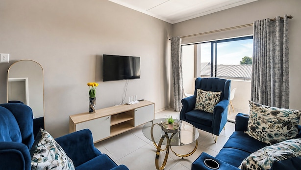 Uma sala de estar moderna com televisão de tela plana, um conjunto de sofás, uma mesa de centro e vista para o exterior através de grandes janelas.