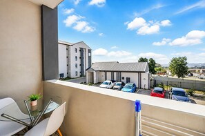 A balcony with a glass table and chairs, overlooking a parking area with several cars and a building in the background. - Luxury 2 bedroom, 2 bathroom apartment in Carlswald with swimming pool. (Midrand)