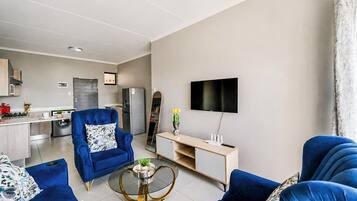 A modern living room with a blue sofa set, a coffee table, and a flat-screen TV mounted on the wall.