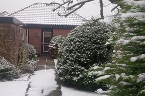 Un sentier enneigé mène à une maison en briques surmontée d’un toit en tuiles.