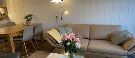 Una sala de estar con un sofá, una mesa de comedor con sillas y una mesa de centro con un jarrón de flores.