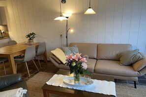 Ein Wohnzimmer mit einer Couch, einem Esstisch mit Stühlen und einem Couchtisch mit Blumen.