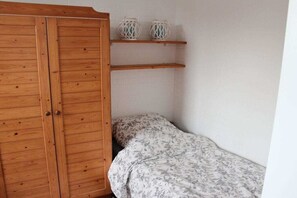 Une chambre avec une armoire en bois, un lit avec une literie à motifs floraux et deux étagères ornées d’objets décoratifs.