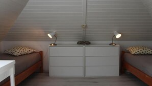 Quarto com duas camas, penteadeira branca e duas luminárias de cabeceira.