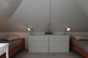 Een slaapkamer met twee bedden, een witte dressoir en twee bedlampjes.