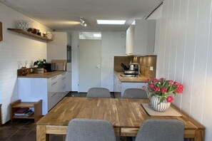 Eine kompakte Küche mit weißen Schränken, einem Holztisch und einer Blumenvase.