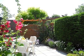 Een terras met een houten pergola, witte stoelen en verschillende planten.