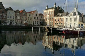 Un canal où les bâtiments se reflètent dans l’eau, un quai avec un bateau, et un ciel dégagé.