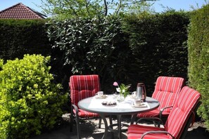 Een ronde tafel met stoelen, een theepot, kopjes en een bloemstuk.