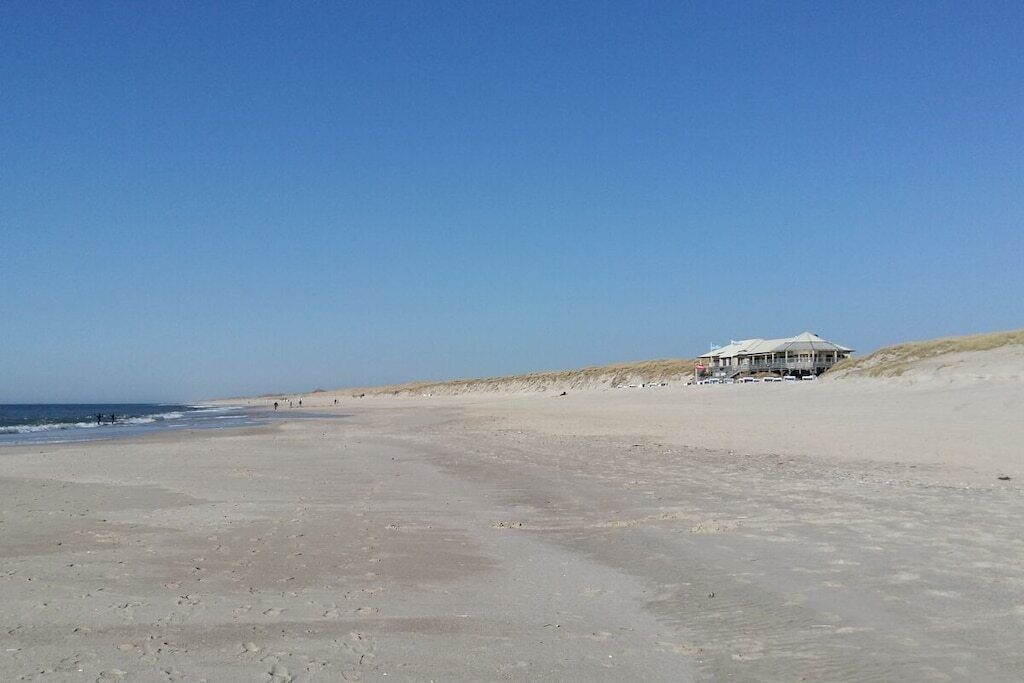 A beach with a building that has a flat roof and multiple windows.