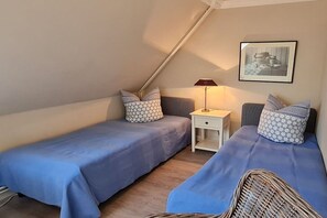 Quarto com duas camas de solteiro, mesa de cabeceira, luminária e quadro na parede.