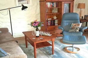 Un salon avec une table basse en bois, un fauteuil bleu, une bibliothèque et un lampadaire.