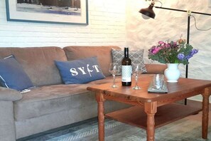 Ein gemütlicher Wohnbereich mit einer Couch, einem Couchtisch, einer Weinflasche, Gläsern und einer Vase mit Blumen.